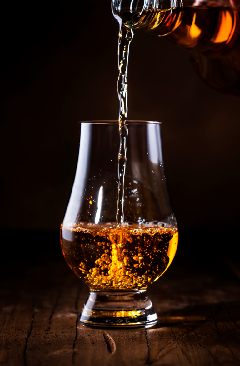 Macro atmospheric detail of amber liquid pouring into high-end glassware, casting warm reflections to highlight exclusive membership hospitality.